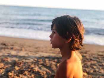 Profile view of thoughtful shirtless boy standing at beach