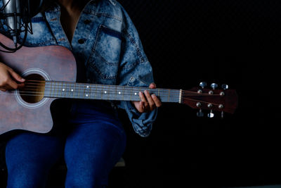 Midsection of man playing guitar against black background