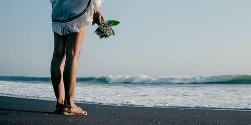 Low section of woman standing on beach against sky