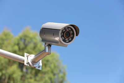 Low angle view of security camera against clear blue sky