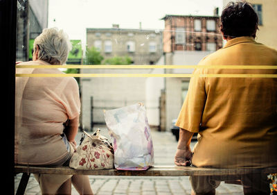 Rear view of man and woman sitting on bench seen through window glass