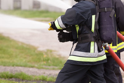 Midsection of firefighters spraying water from hose