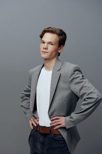 Portrait of young man standing against gray background