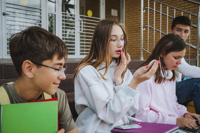 Teenage girl doing makeup with friends sitting on steps