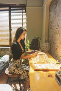 Side view of young woman sitting on table at home