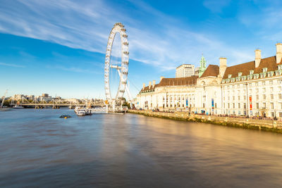 Ferris wheel by river against buildings in city