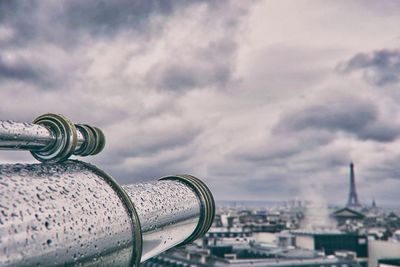 Close-up of cityscape against cloudy sky with telescope