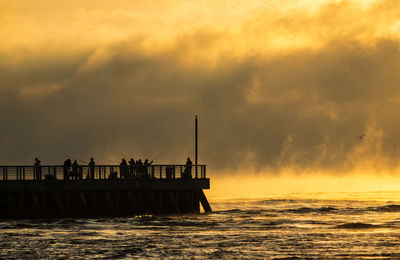 Silhouette people on pier at sea against sky during sunset