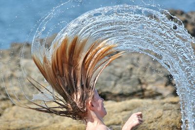 Close-up of woman splashing water with wet hair at lakeshore