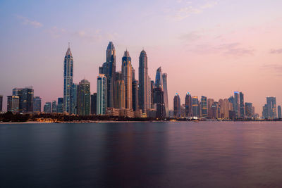 City at waterfront against sky during sunset