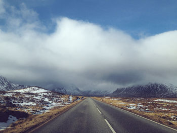 Scenic view of road passing through snowy landscape against cloudy sky