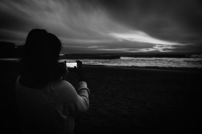 Rear view of woman photographing sea through mobile phone during sunset