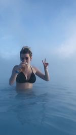 Portrait of young woman drinking beer in sea during foggy weather