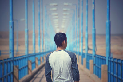 Rear view of man standing by railing against bridge