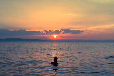 Silhouette person swimming in sea at sunset
