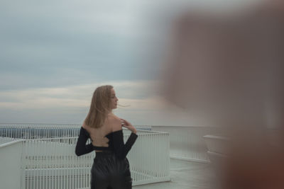 Rear view of woman standing against railing against sky