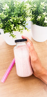 Cropped hand of person holding drink in bottle on table