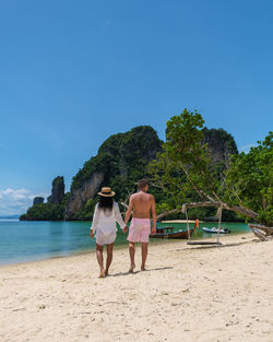 Rear view of woman walking at beach against clear blue sky