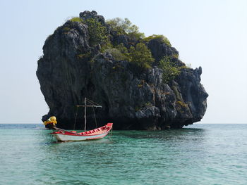 Boat on sea by rock formation against clear sky