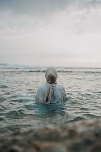 Rear view of woman in hijab enjoying in sea at beach against sky