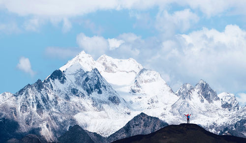 Distant view of hiker standing on mountain against cloudy sky