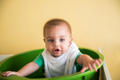 Portrait of cute baby boy sitting in bucket at home