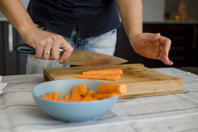 Midsection of woman cutting carrot on board