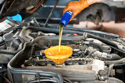 Cropped hand of mechanic pouring oil in car engine