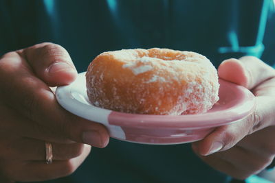 Close-up of hand holding donut in plate