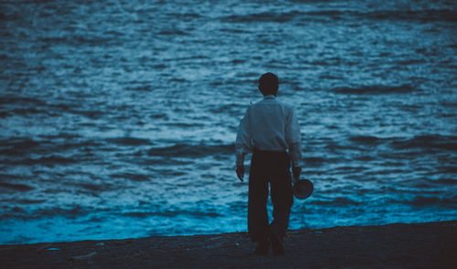 Rear view of man walking towards sea during sunset