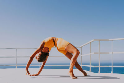 Low section of woman doing yoga at beach against clear sky