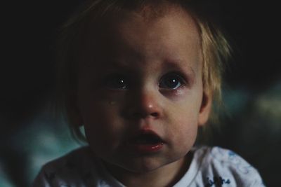 Close-up of cute sad boy crying in darkroom