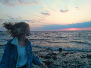 Woman standing at beach against sky during sunset