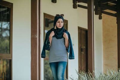 Portrait of young woman standing against building