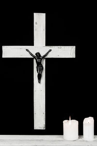 Candles by cross against black background