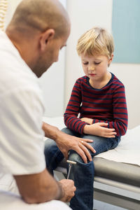 Doctor checking knee reflexes of boy at orthopedic clinic