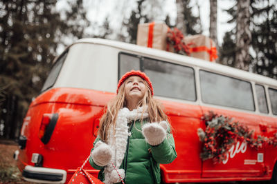 Cute smiling girl standing against car during winter