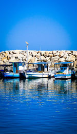 Boats in calm blue sea against clear sky