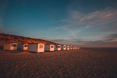 Huts at beach against blue sky during sunset