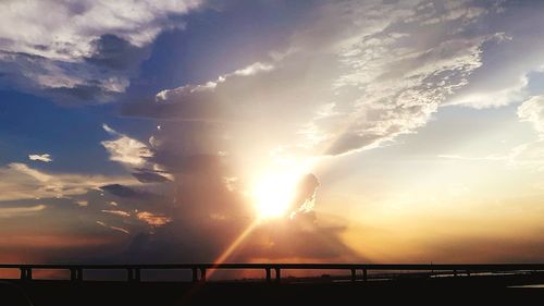 Sunlight streaming through silhouette bridge against sky during sunset