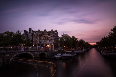 Illuminated bridge over river in city against sky at sunset