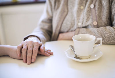 Midsection of senior woman lays her hand on another at home