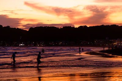 Silhouette people on beach against sky during sunset