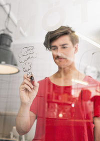 Young businessman drawing clouds on transparent glass in creative office