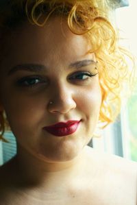 Close-up portrait of shirtless woman with curly blond hair wearing red lipstick