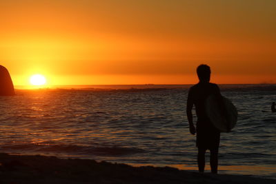 Silhouette man standing on beach against orange sky