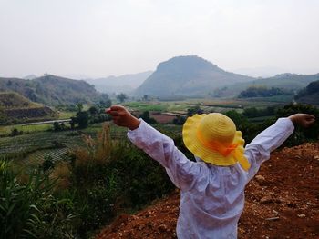 Midsection of woman with arms raised standing on field against sky