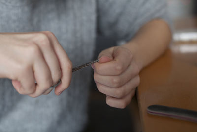 Midsection of woman cutting fingernail with scissors