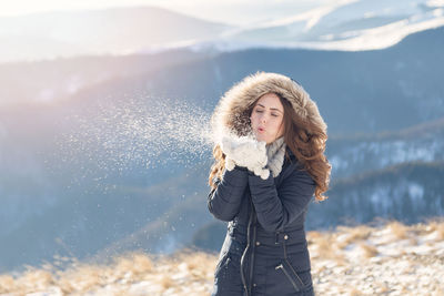 Cheerful woman wearing fur coat while standing against mountains during winter