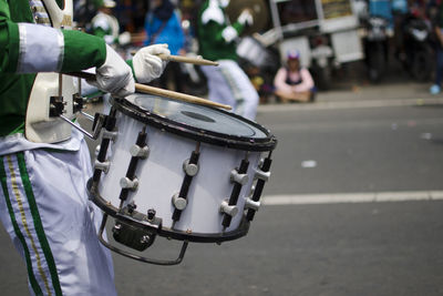 Midsection of musician playing drum on road in city